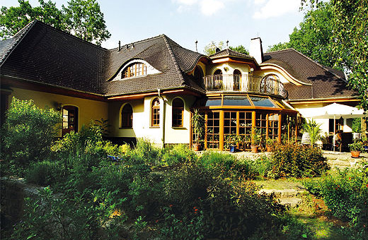 Ein Winkelhaus als Walmdach-Haus in bayerischen Landhaus-Stil mit Holz-Wintergarten und Halbturm über dem Balkon.